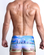 Back view of a Male model wearing swim trunks for men in a Miami and sunny skies print by the Bang! Clothes brand of men's beachwear.