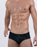 Front view of a male model wearing BANG! Written in the Stars Swim Briefs – black swimwear with glow-in-the-dark green constellation print, designed for a snug, low-rise fit.