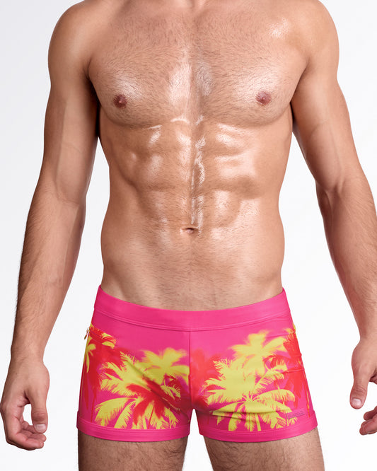 BANG Wuthering Heights Fucsia Swim Trunks — model wearing fitted men’s swim trunks featuring neon yellow palm silhouettes over a bold fucsia pink base.