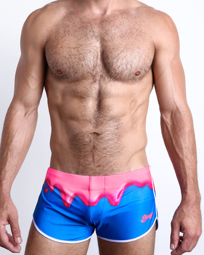 Frontal view of a sexy male model wearing men’s YOU MELT ME swimsuit in a bright blue color featuring strawberry pink melting ice cream print by the Bang! Menswear brand from Miami.