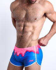 Side view of a masculine model wearing men’s swimwear featuring hot pink melting ice cream print with official logo of BANG! Brand in pink.