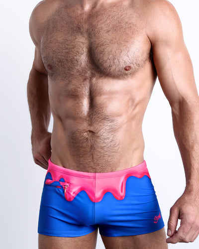 Frontal view of a sexy male model wearing men's swimsuit with mini pockets in YOU MELT ME in a bright blue color featuring pink melting ice cream print designed by the Bang! Menswear brand from Miami.