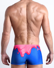 Back view of a Male model wearing swim trunks for men featuring magenta pink melting ice cream print by the Bang! Clothes brand of men's beachwear.