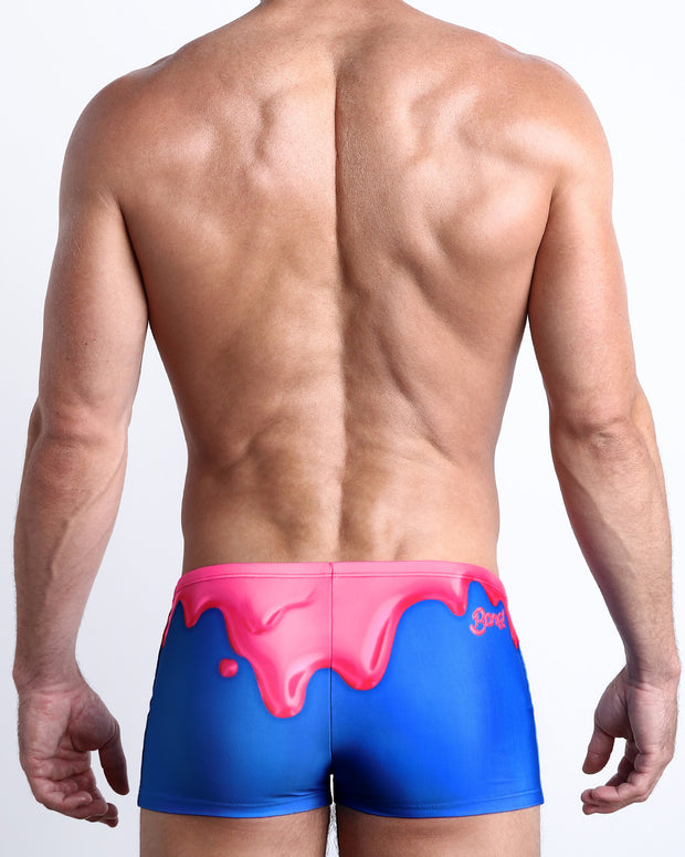 Back view of a Male model wearing swim trunks for men featuring magenta pink melting ice cream print by the Bang! Clothes brand of men&