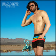 Front view of a sexy male model wearing BANG Miami premium tailored shorts in black with colored stripes red yellow blue lgbtq