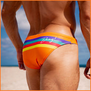 Back view of male model wearing a swim mini-brief in vibrant orange with color stripes in yellow, bold red, aqua, and blue.