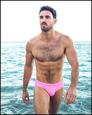 Front view of a sexy male model wearing BANG Miami pink swim brief in a beach setting hot summer body 2021 lgbtq best mens swimwear