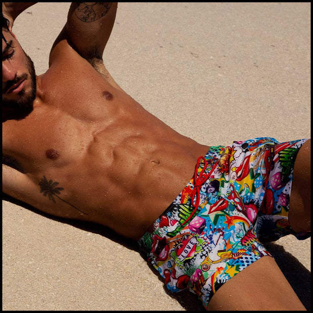 Front view of a sexy male model wearing BANG Miami premium Flex shorts in yeah yeah print unique comics red green blue white yellow
