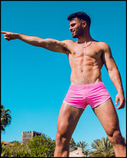 Front view of a sexy male model wearing BANG Miami pink swim shorts in a beach setting hot summer body lgbtq best mens swimwear