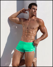 Male model outdoors wearing the AQUA GLOW Swim Shorts by BANG! Clothes the official brand of men’s swimwear.