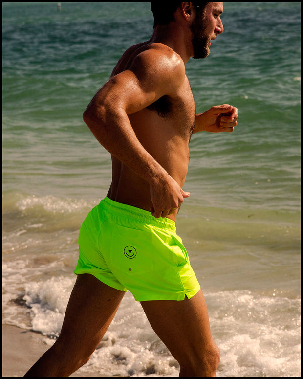 Model wearing men’s swim trunks in neon highlighter yellow color by the Bang! Clothes brand of men&