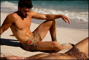 View of a sexy model at the beach wearing the CATS N'ROSES men’s swim bottoms featuring leopard print in brown tones with red roses by the Bang! menswear brand from Miami.