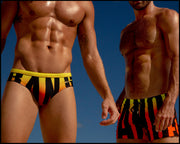 View of muscular male models wearing BIG BANG GOLDEN HOUR matching Summer swimsuits for the beach with a bright red, orange and yellow gradient background.