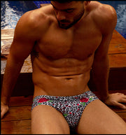 Male model's sitting down view showing the SO RED THE ROSE beach mini-briefs for men featuring animal print of black and white cheetah with red roses by Bang! men's swimwear.