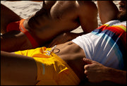 Model laying down at the beach wearing the RADIANT YELLOW men’s swim shorts in yellow color by the Bang! brand of men's beachwear from Miami. Next, another model wearing the BRONZE FACTOR Swim Mini-Brief. 
