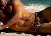 Male model's laying out by the ocean showing the CATS N'ROSES square leg swim trunks for men featuring animal print of brown cheetah with red roses by Bang! men's swimwear.