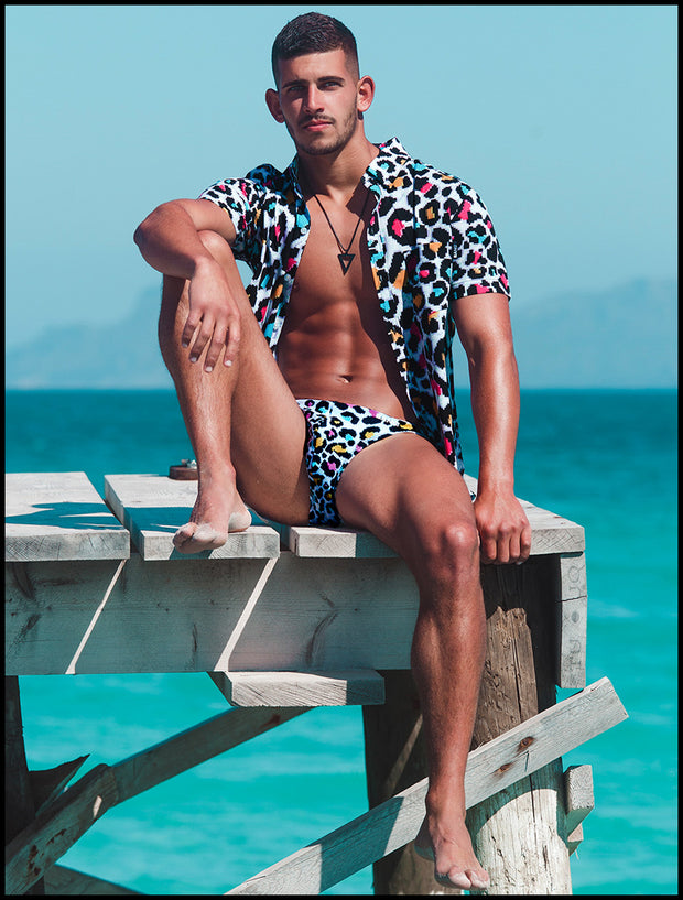 Male model sitting down by the ocean wearing the 8-BIT POP LEOPARD Summer button down by Bang! Clothes multi-colored leopard animal print.
