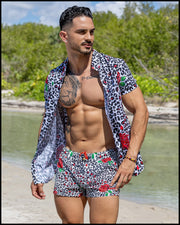 Model at the beach wearing the SO RED THE ROSE men’s short-sleeve stretch shirt and matching Mini Shorts featuring leopard print in white and black tones with red roseswith matching Show Shorts  by the Bang! menswear brand.