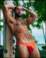 Sexy male model outdoors by the showers wearing a men's bikini-style bottoms in tangerine color by the Bang! Menswear brand from Miami.