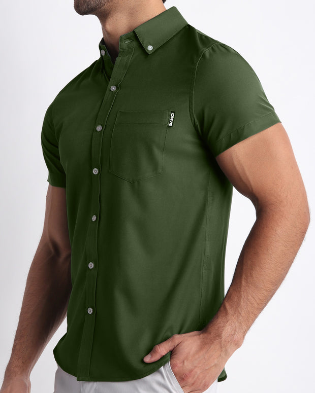 Side view of a masculine model wearing men’s ALPHA GREEN Summer button down shirt in a forest green color with official logo of BANG! Brand.