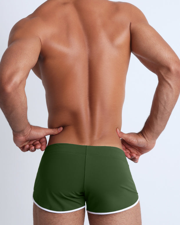 Back view of a male model wearing men’s swim shorts in smooth hunter green color by the Bang! Clothes brand of men&