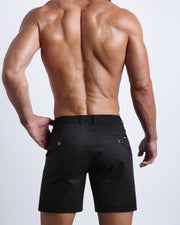 Back view of a model wearing woven twill cotton chino shorts in black color for men by BANG! Clothing brand of Miami.