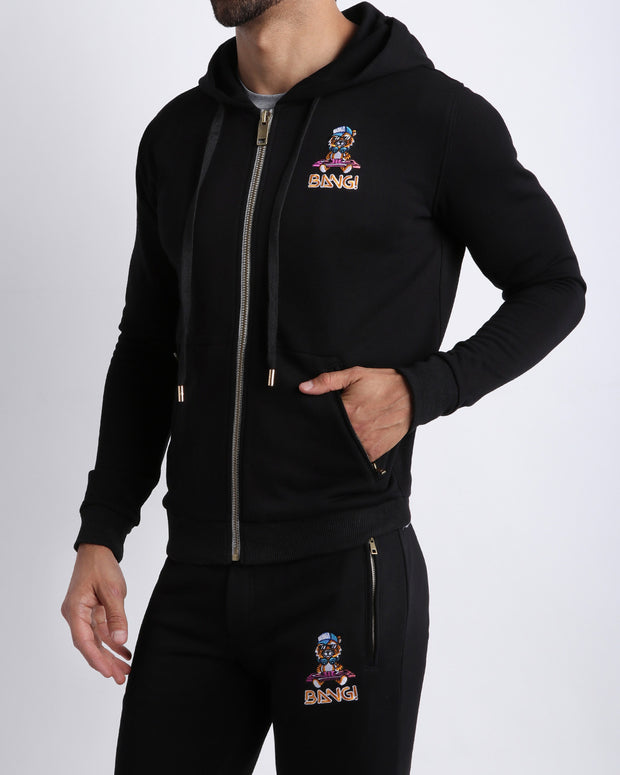 Frontal view of male model wearing the BANG! Clothes BLACK Tracksuit Hoodie Jacket with frontal zipper closure. This long-sleeve jacket has an embroidered Bang! Logo with the signature Mister TJ tiger. 