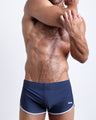 Frontal view of a sexy male model wearing men’s swimsuit in dark blue color by the Bang! Menswear brand from Miami.