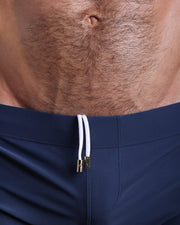 Close-up view of men’s summer beach shorts by BANG! clothing brand, showing white cord with custom branded golden cord ends, and matching custom eyelet trims in gold.