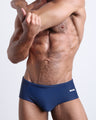 Frontal view of a sexy male model wearing men’s swimsuit in BLUE JEAN a dark blue color color by the Bang! Menswear brand from Miami.