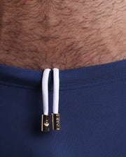 Close-up view of the BLUE JEAN Swim Sunga mens swimsuit a dark blue color with white internal drawstring cord showing custom branded golden buttons by BANG! clothing brand.