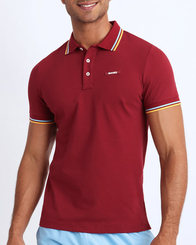 Front view of a sexy male model wearing a premium 100% Cotton Pique Polo Shirt for men from BANG! Brand in a dark red color.