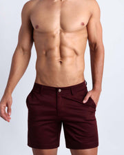 Front view of a male model wearing men's chino shorts in bold dark red color with cuff in stripes light blue, yellow and red color by BANG! Miami Clothes brand.