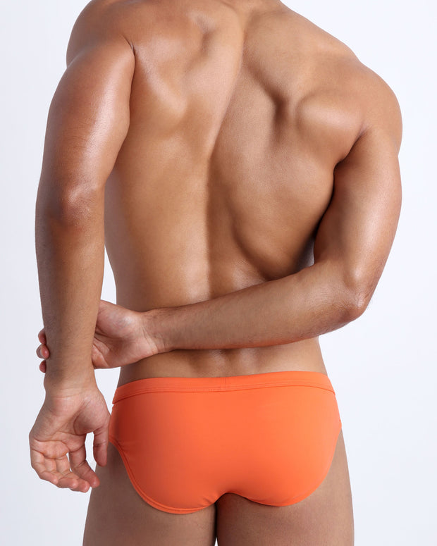 Back view of a male model wearing men’s swim briefs in apricot color by the Bang! Clothes brand of men&