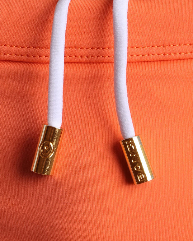 Close-up view of men’s summer swimwear by BANG! clothing brand, showing white cord with custom branded golden cord ends, and matching custom eyelet trims in gold.