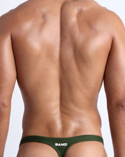 Back view of a male model wearing men’s swim thongs made with Italian-made Vita By Carvico Econyl Nylon in smooth hunter green color by the Bang! Clothes brand of men's beachwear.