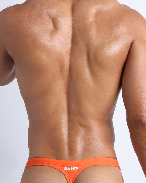 Back view of a male model wearing men’s swim thongs in apricot color by the Bang! Clothes brand of men&