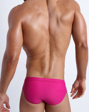 Back view of a male model wearing men’s swim briefs in bright ruby color by the Bang! Clothes brand of men's beachwear.