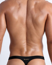 Back view of a male model wearing men’s bikini swimwear in smooth black color by the Bang! Clothes brand of men's beachwear.