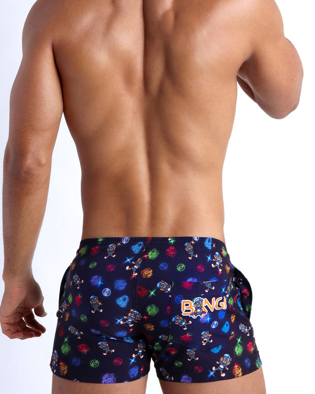 Back view of model wearing the HEY MISTER TJ (CLUB MIX) Men’s beach trunks by BANG! with clubbing and disc-jockey details in dark colors.