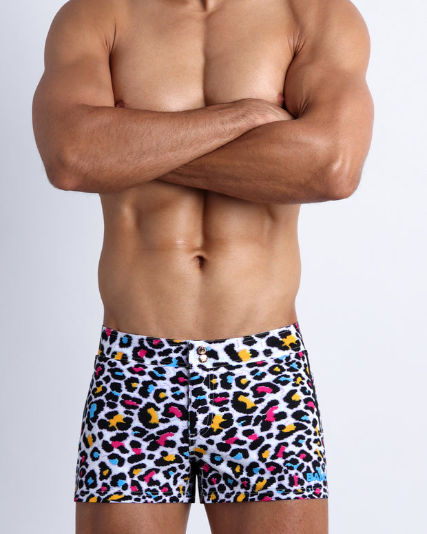Male model wearing the 8-BIT POP LEOPARD men’s swim beach shorts in black leopard print with blue, yellow and fuchsia bold colors by Bang! Miami men&
