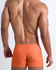 Back view of a male model wearing men’s beach trunks in orange color by the Bang! Clothes brand of men's beachwear.