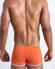 Back view of a male model wearing men’s swim shorts in apricot color by the Bang! Clothes brand of men's beachwear.
