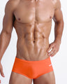 Frontal view of a sexy male model wearing a men's brief-style bottoms in tangerine color by the Bang! Menswear brand from Miami.