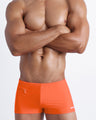 Frontal view of a sexy male model wearing a men's swimsuit with mini pockets in tangerine color by the Bang! Menswear brand from Miami.