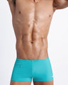 Frontal view of a sexy male model wearing men’s swimsuit with mini pockets in cerulean blue color by the Bang! Menswear brand from Miami.