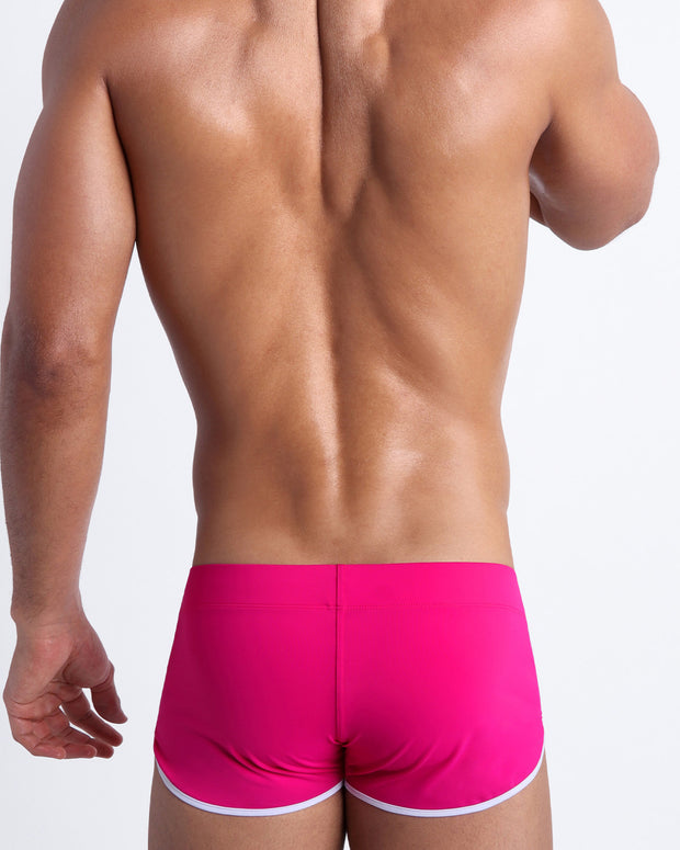 Back view of a male model wearing men’s swim shorts in bright ruby color by the Bang! Clothes brand of men&