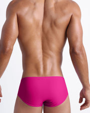 Back view of a male model wearing men’s swim sunga made with Italian-made Vita By Carvico Econyl Nylon in bright fuchsia color by the Bang! Clothes brand of men's beachwear.