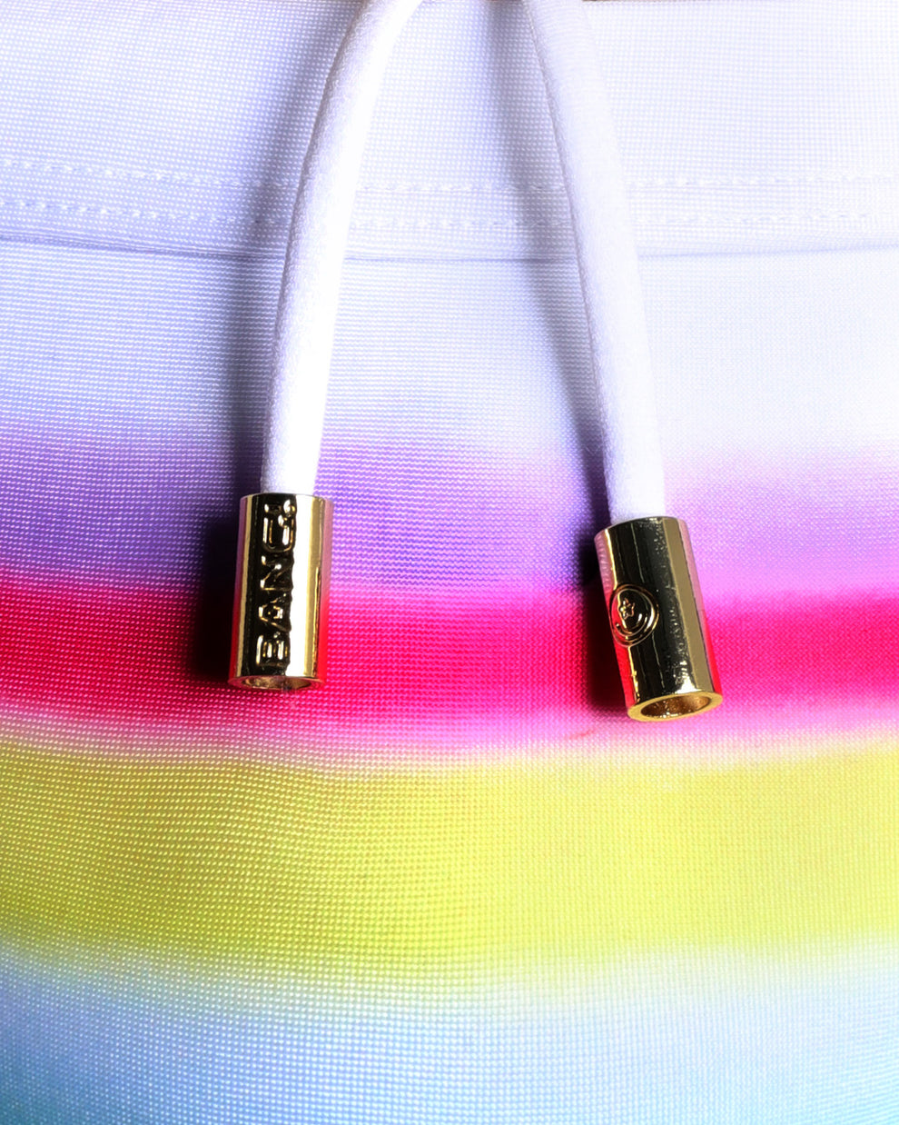 Close-up view of men’s summer swimwear with a rainbow, showing white cord with custom branded golden cord ends, and matching custom eyelet trims in gold.