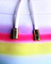 Close-up view of men’s summer swimwear with a rainbow, showing white cord with custom branded golden cord ends, and matching custom eyelet trims in gold.